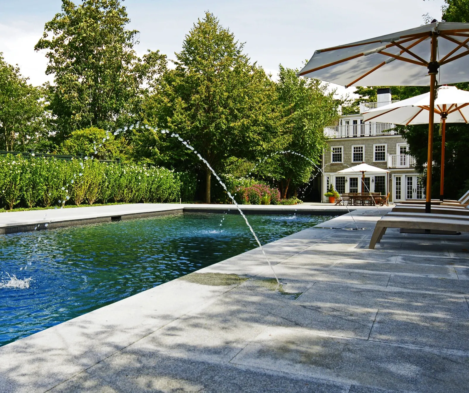 Pool with deck jets arcing into the water beside a stone deck