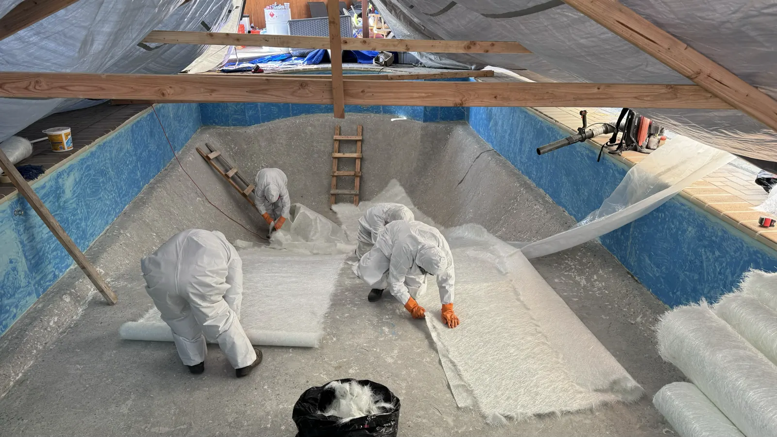 Crew laying fiberglass mat to resurface a pool