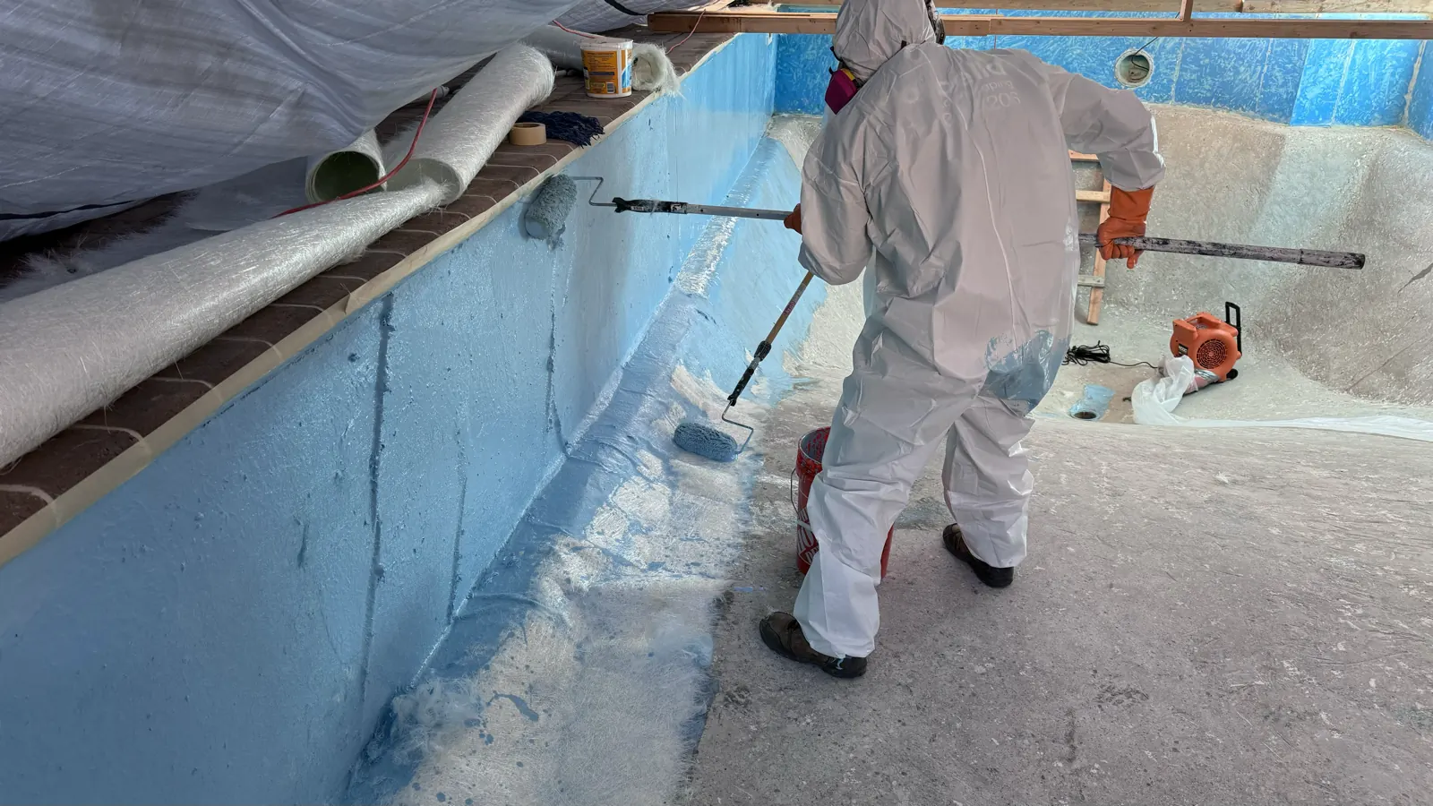 Technician rolling resin onto the wall of a pool being resurfaced